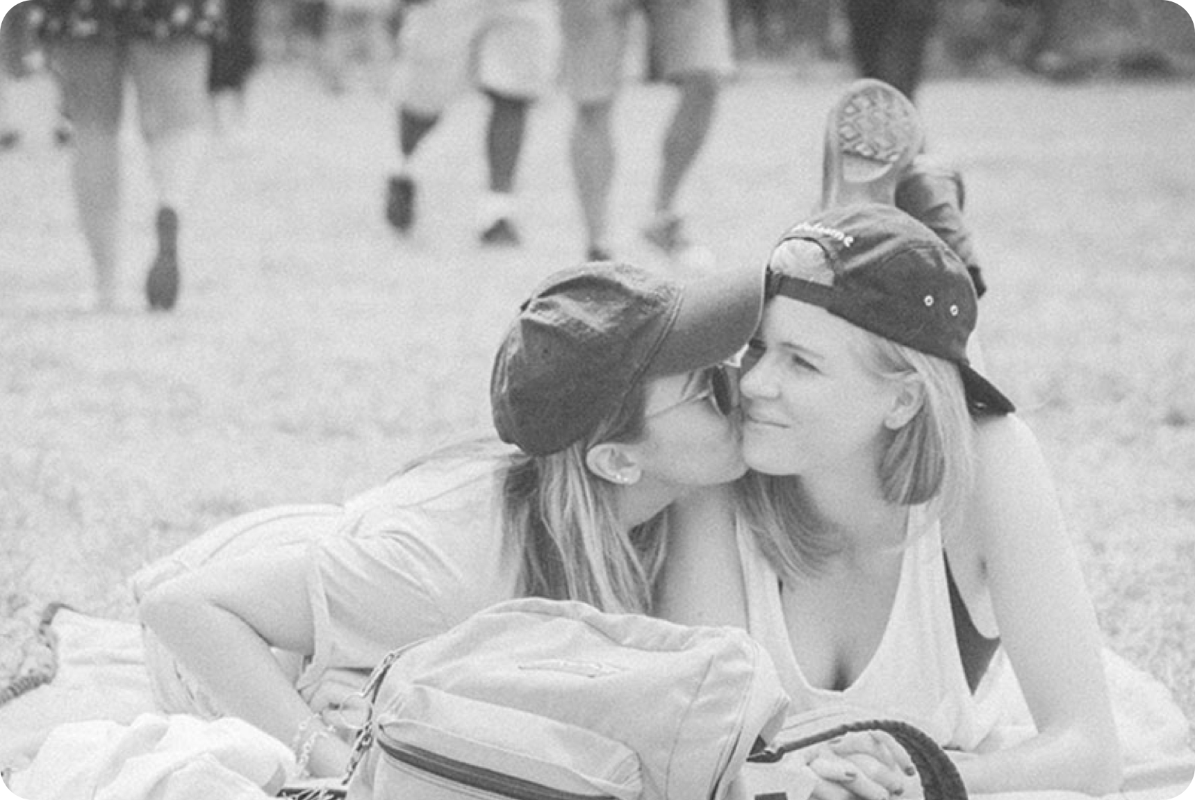 A girl kisses another girl on the cheek lying on the grass 