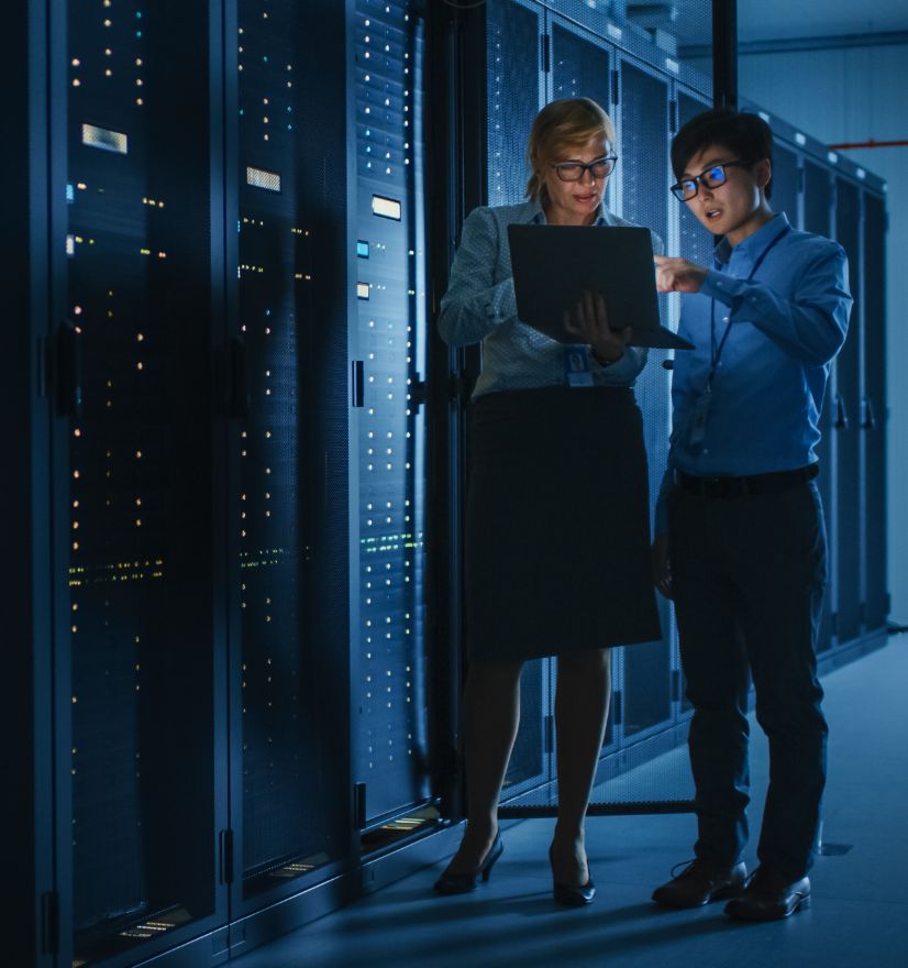One female and  one male IT worker looking at a laptop in front of servers.