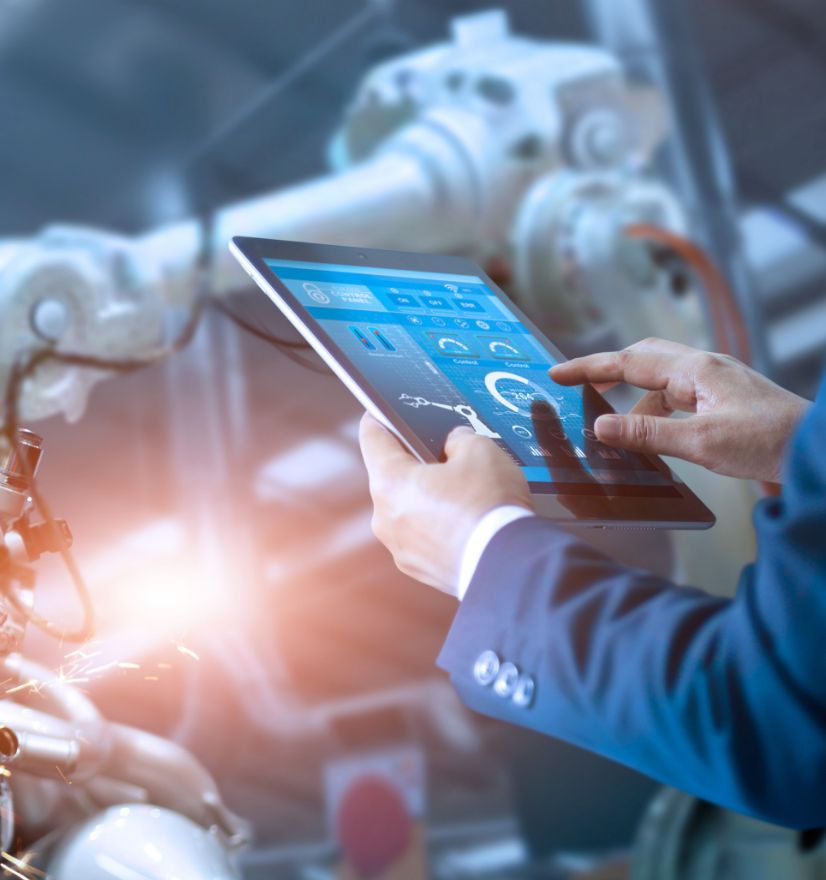 Factory worker's hands using tablet with robotic arms in the background.