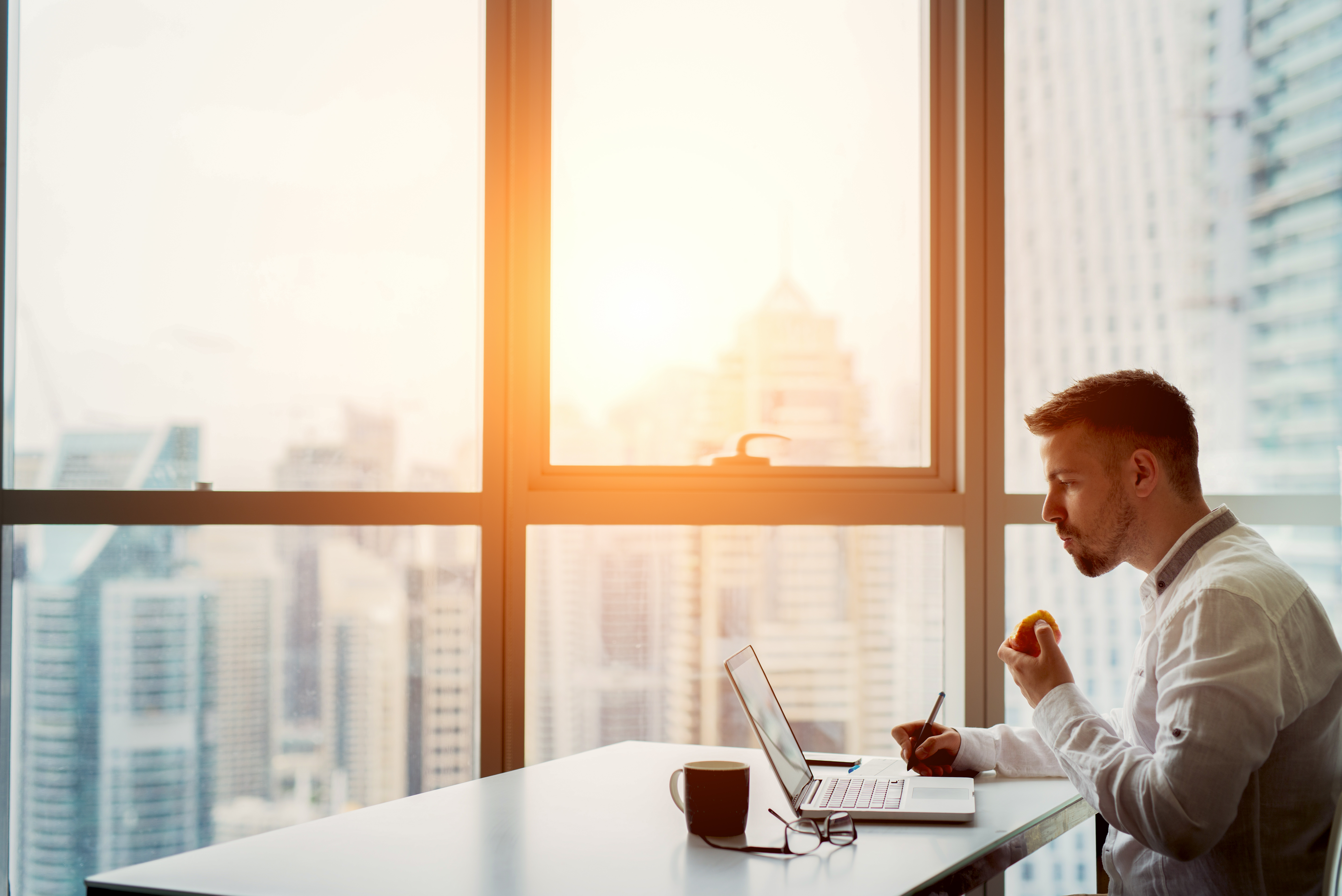 Man sitting at table next to panoramic window with magnificent city view. Sunset light.