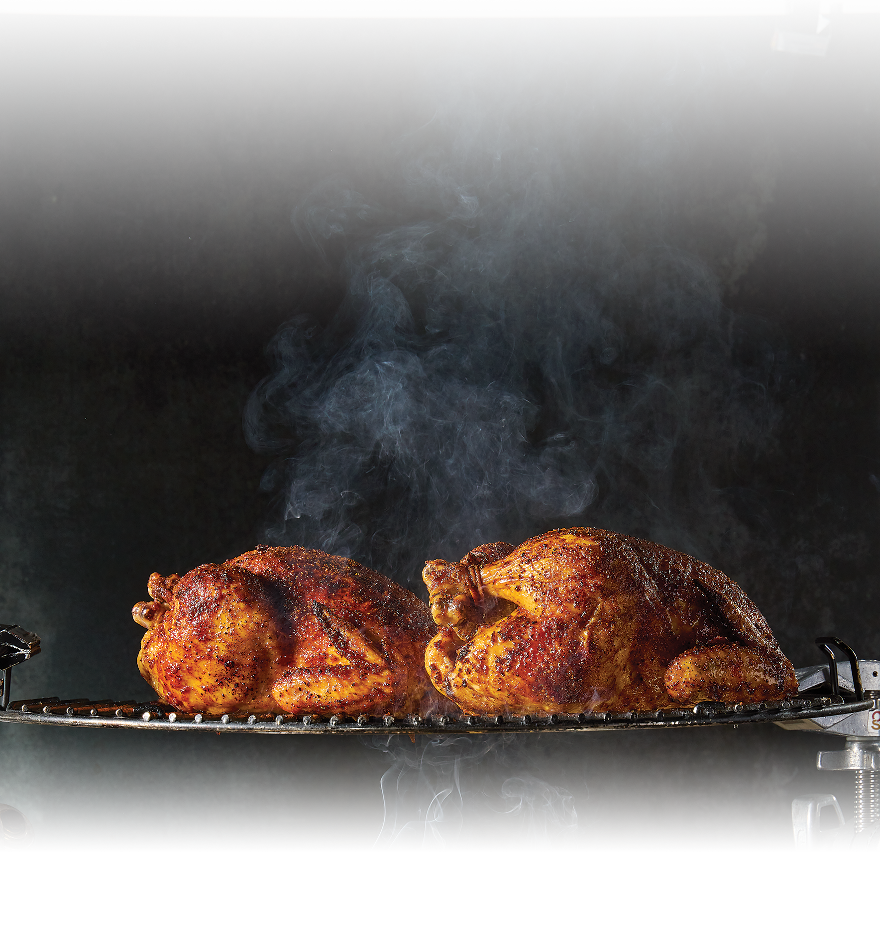 Two whole chickens smoked and sitting on a grill steaming hot.