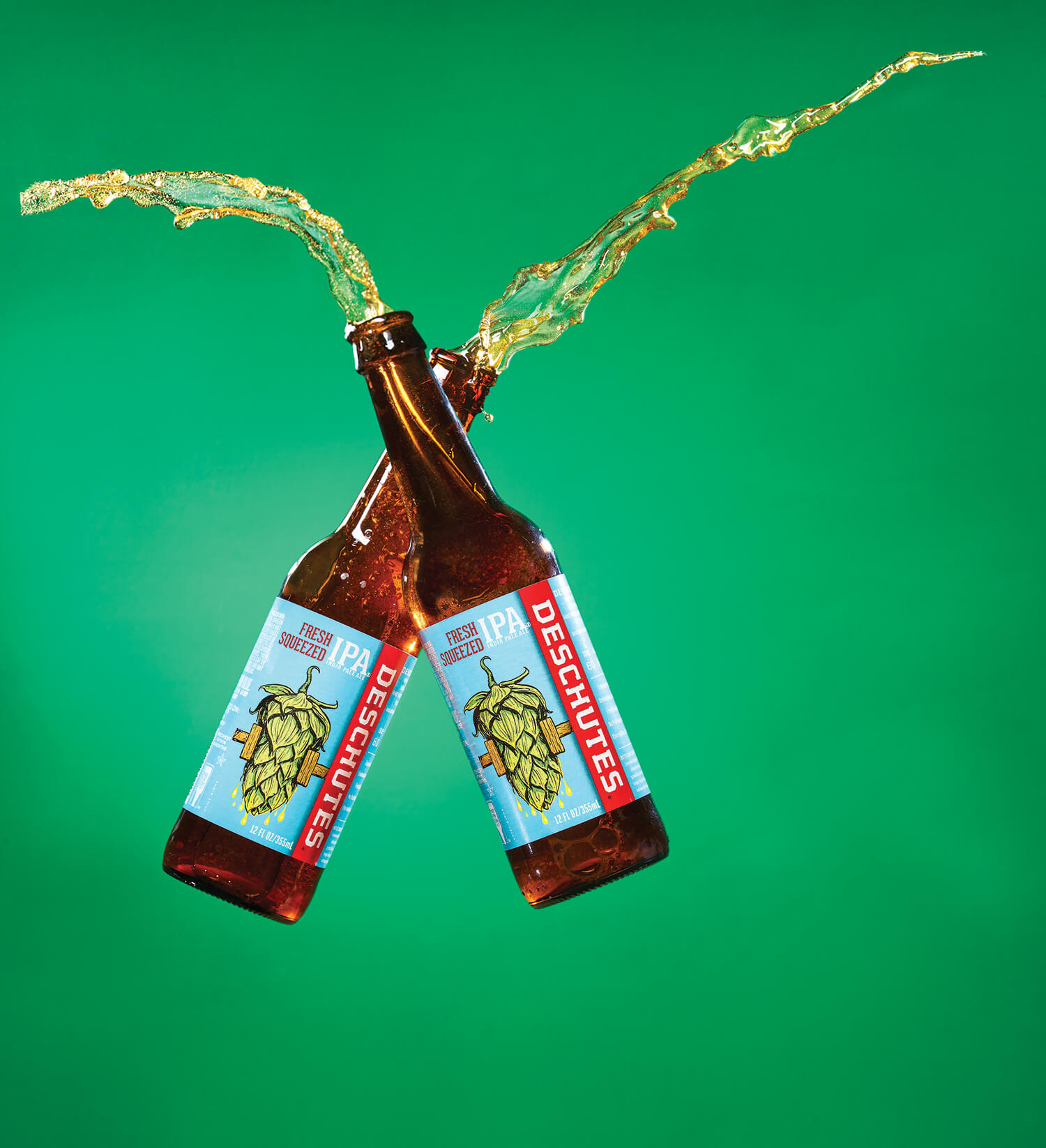 Two Deschutes Fresh Squeezed IPAs Splashing as they Cheers Together Over Green Background