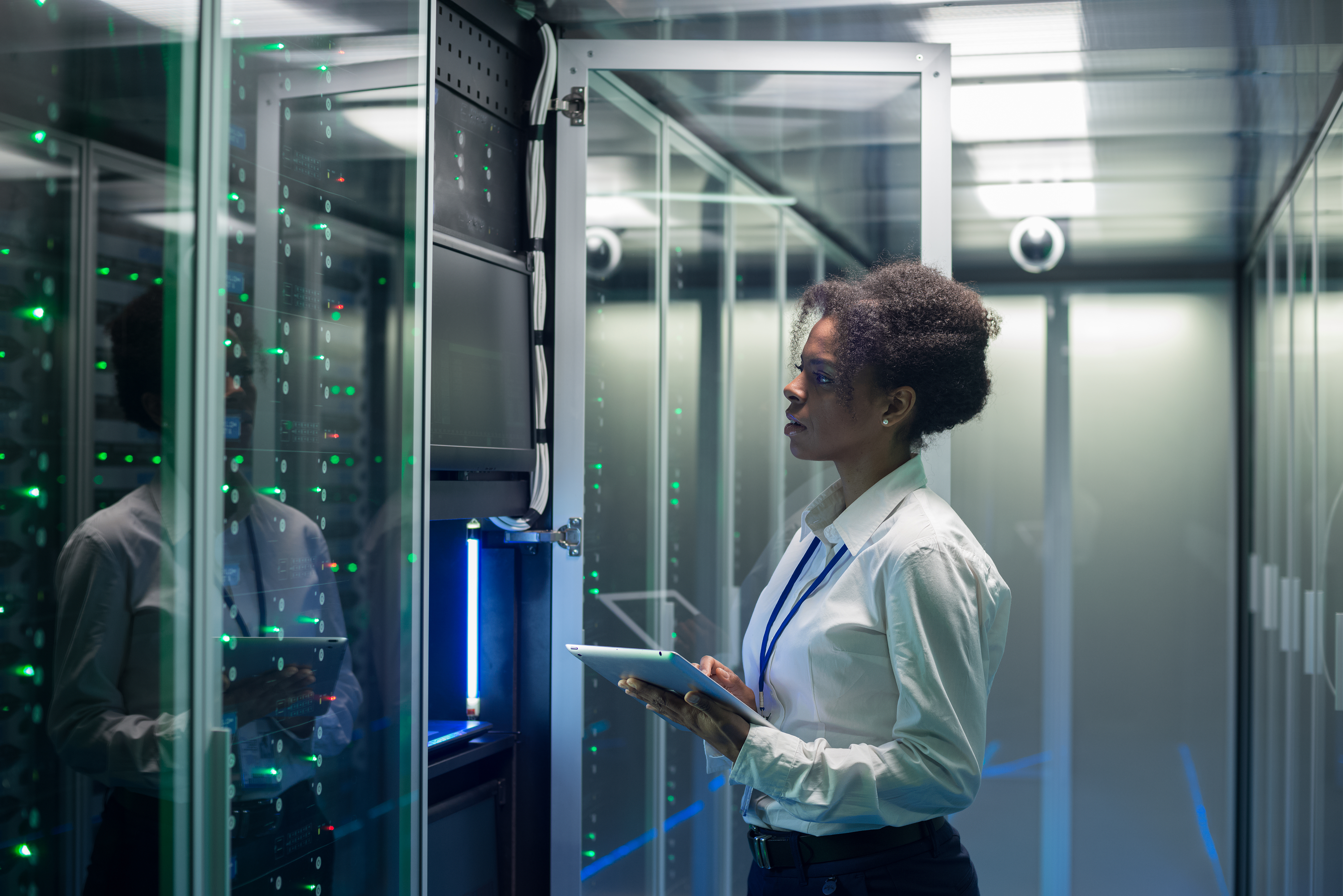 Medium shot of female technician working on a tablet in a data center full of rack servers running diagnostics and maintenance on the system