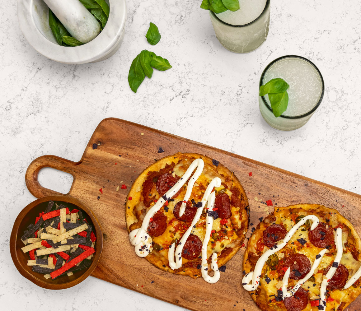 2 glasses of briana's frozen gin smash next to 2 nacho pizzas on a wooden board close up