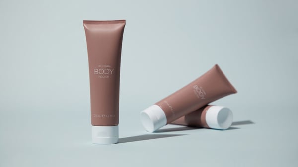 3 Tubes of ageLOC Body polish arranged in various positions on a blue backdrop.