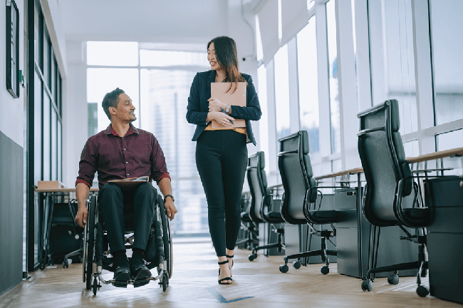 Male worker in wheelchair having cheerful discussion with his female coworker