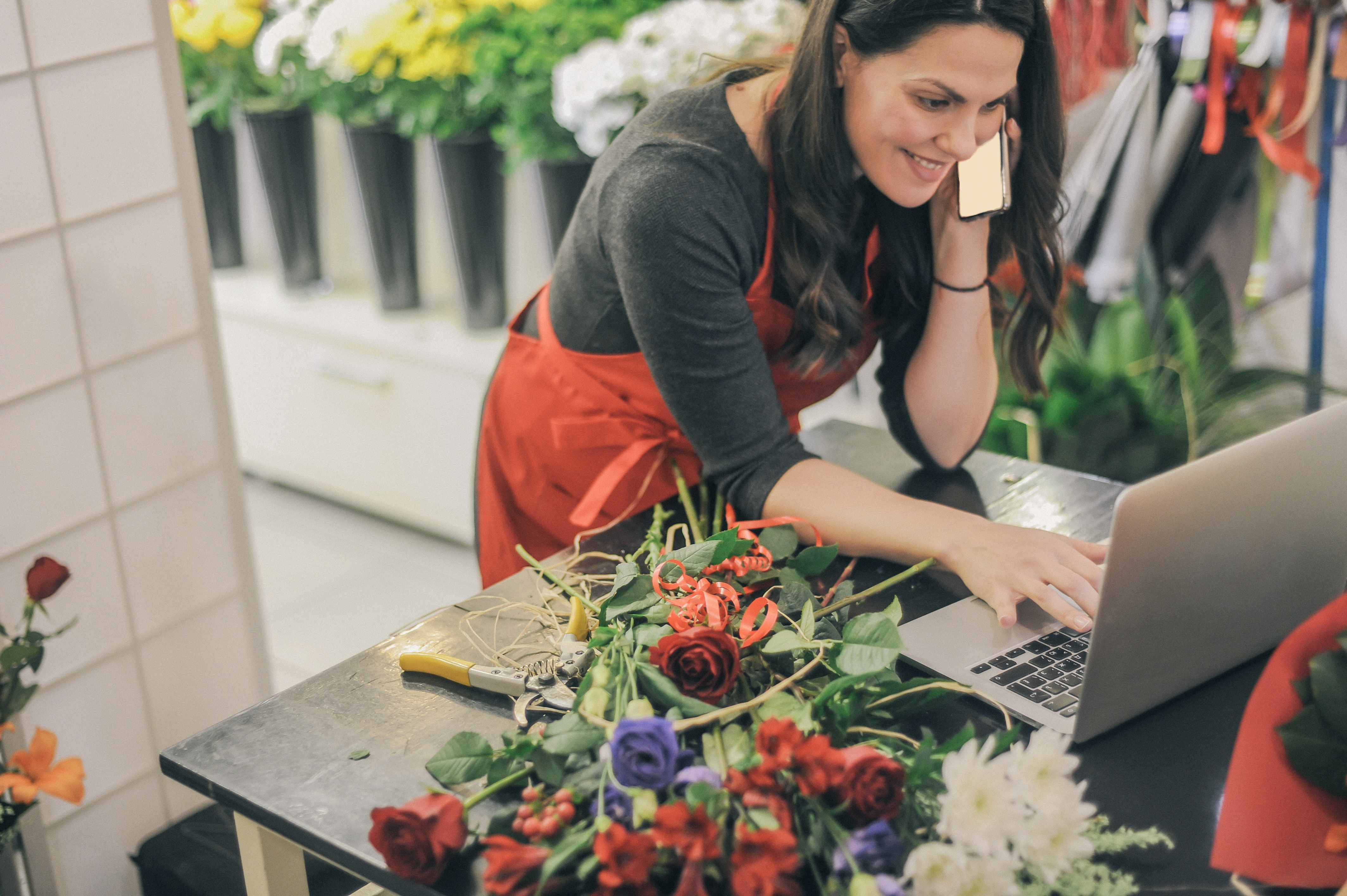 Female owner of flower shop on laptop and talking into a cellphone